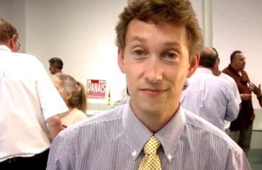 A young man with curly hair smiles in a crowded room