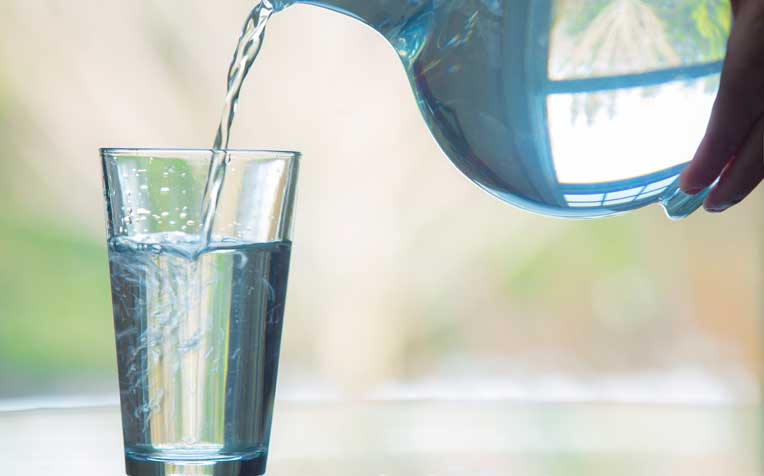 hand pours water from a glass pitcher into a cup