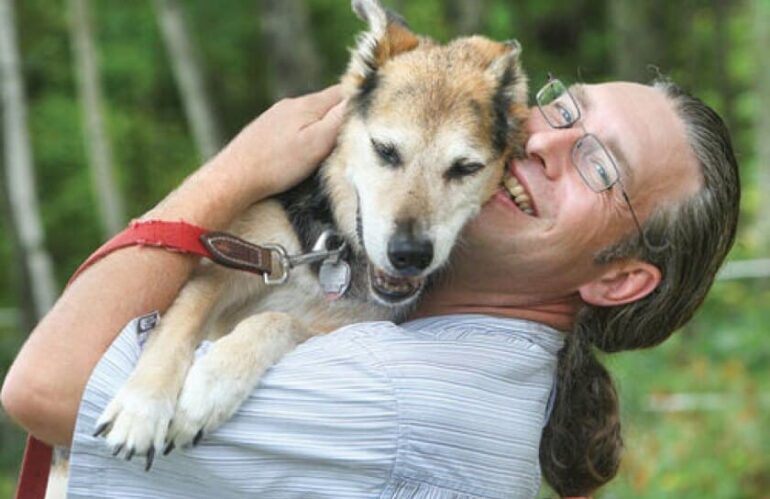 Man with glasses holding a dog in his arms