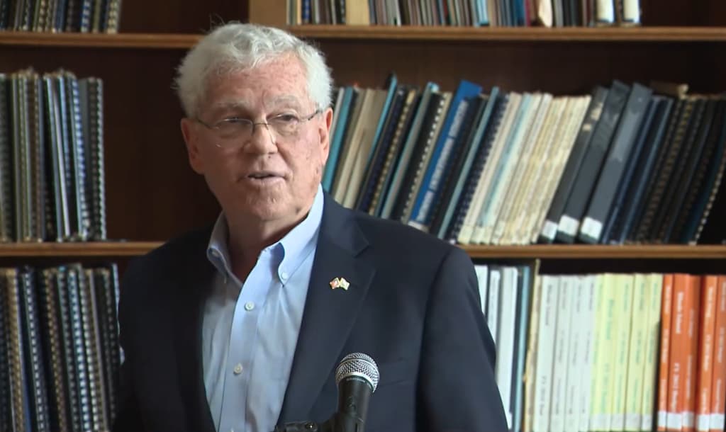 A man in a blazer speaks at a podium with microphones