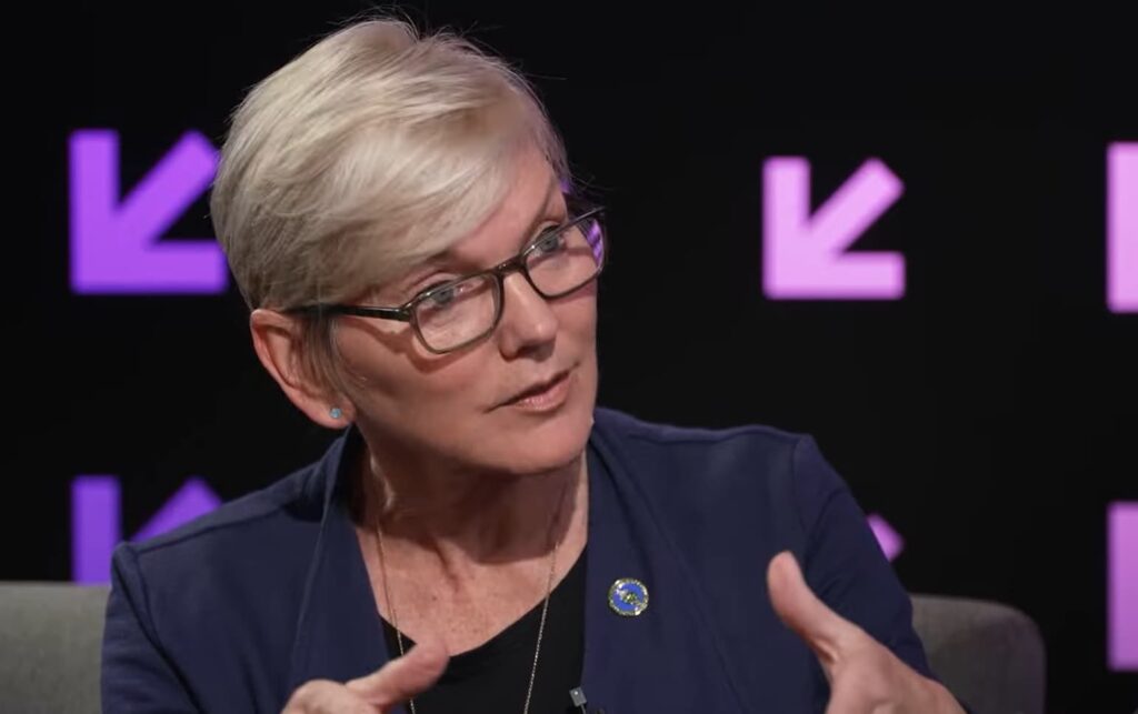 The woman in a navy blazer gestures during a discussion with a purple backdrop